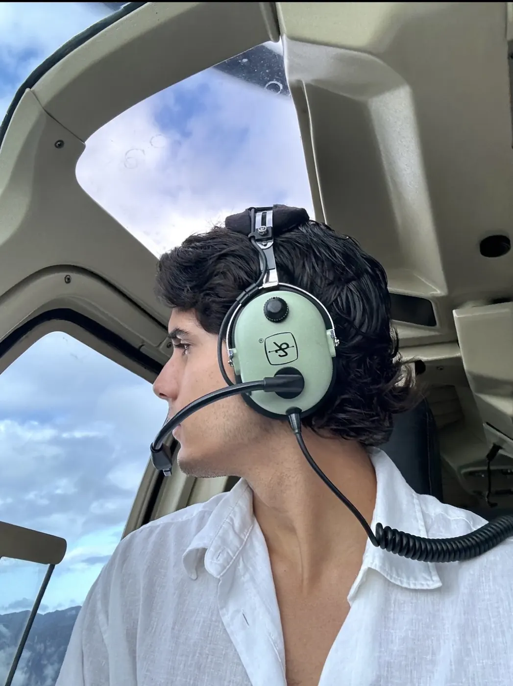 Alex Klaric wearing a pilot headset in a helicopter cockpit above the mountains of Venezuela